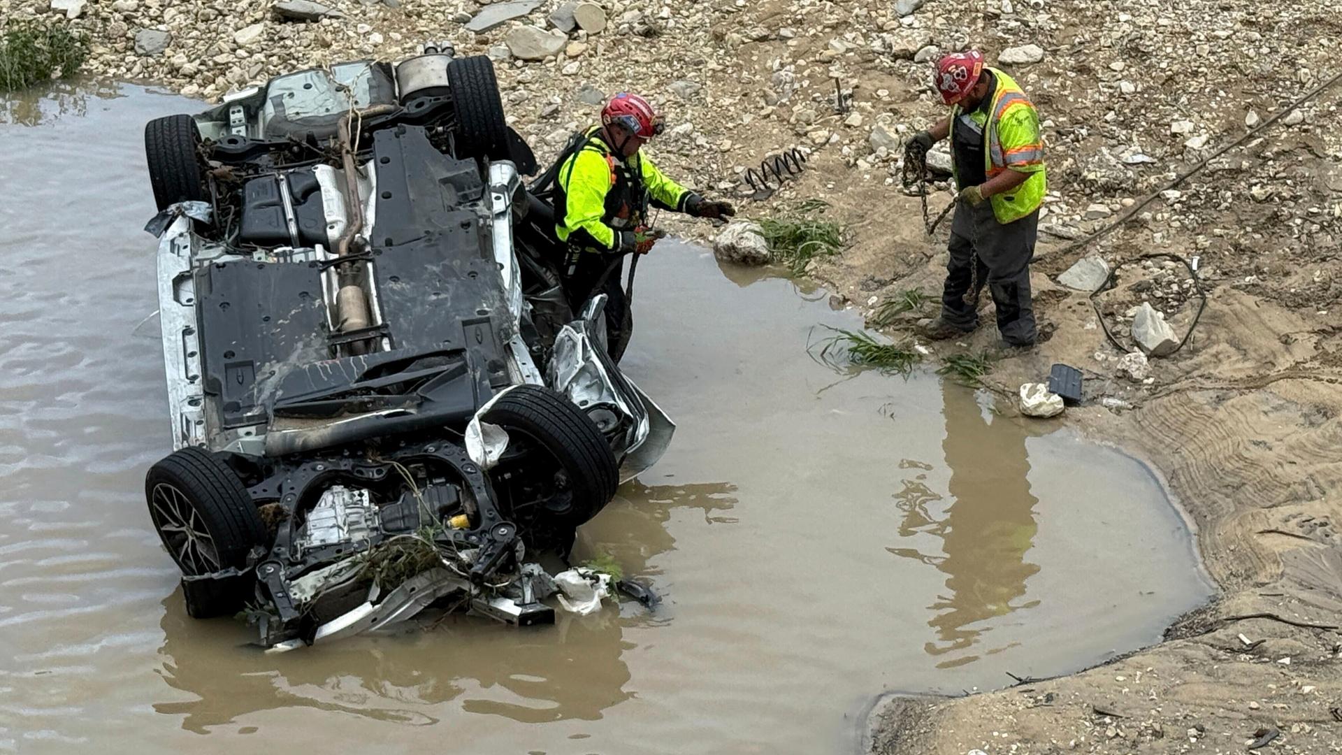Rettungskräfte untersuchen ein Auto, das kopfüber in einem Fluss liegt.