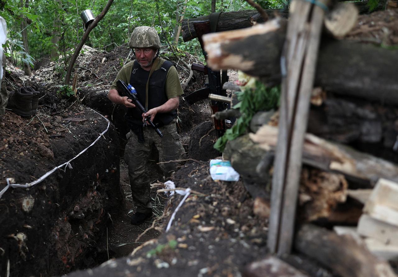 Ein ukrainischer Soldat an der Frontlinie nahe der Stadt Awdijiwka in der Region Donezk. Der Mann steht mit einem Gewehr in einem Schützengraben in einem Waldstück.