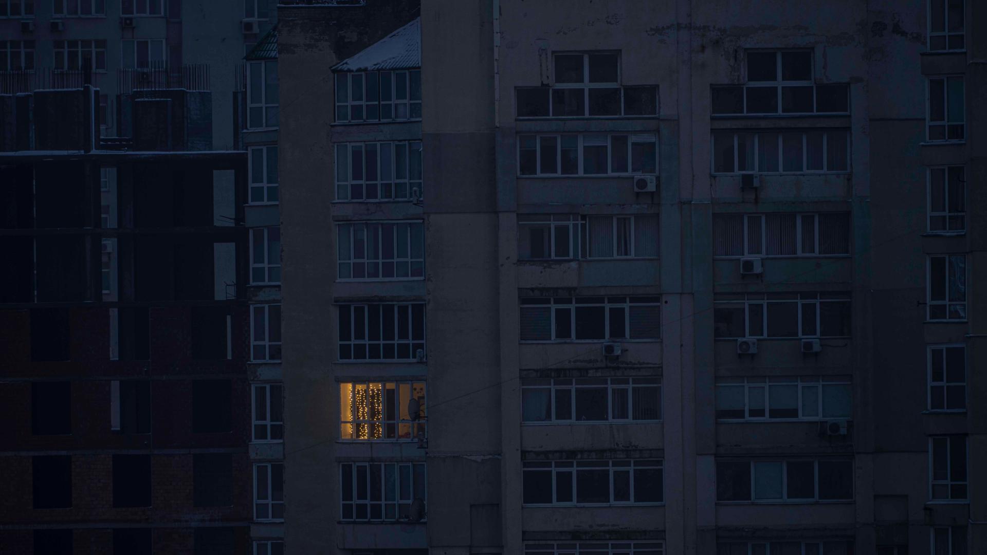 Fensterfront eines Wohnhochhauses in Kiew im Dunkeln - aus einem einzelnen Fenster dringt Licht.