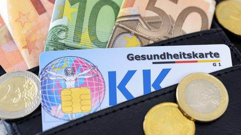 Eine Gesundheitskarte in einer Geldbörse. Darumherum liegen Euroscheine und Münzen.