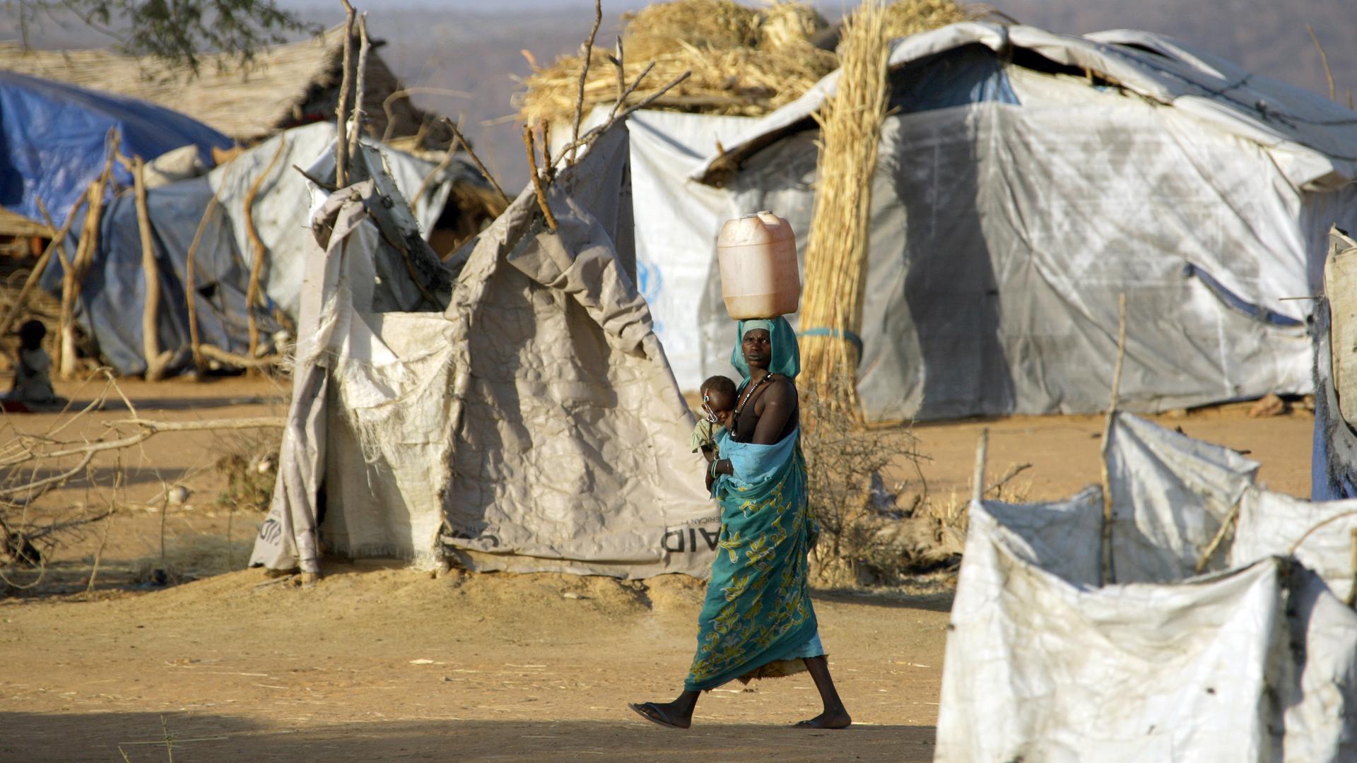 Mit einem Wasserkanister auf dem Kopf und einem Baby im Arm geht eine Flüchtlingsfrau durch ein Füchtlingslager bei Mukjar in West-Darfur im Sudan. Mit einem Wasserkanister auf dem Kopf und einem Baby im Arm geht eine Flüchtlingsfrau durch ein Füchtlingslager bei Mukjar in West-Darfur im Sudan.