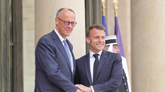 Der Präsident von dem Land Frankreich heißt Emaunnel Macron. Er begrüßt den neu gewählten Bundes-Kanzler Friedrich Merz. Beide reichen sich die Hand.  