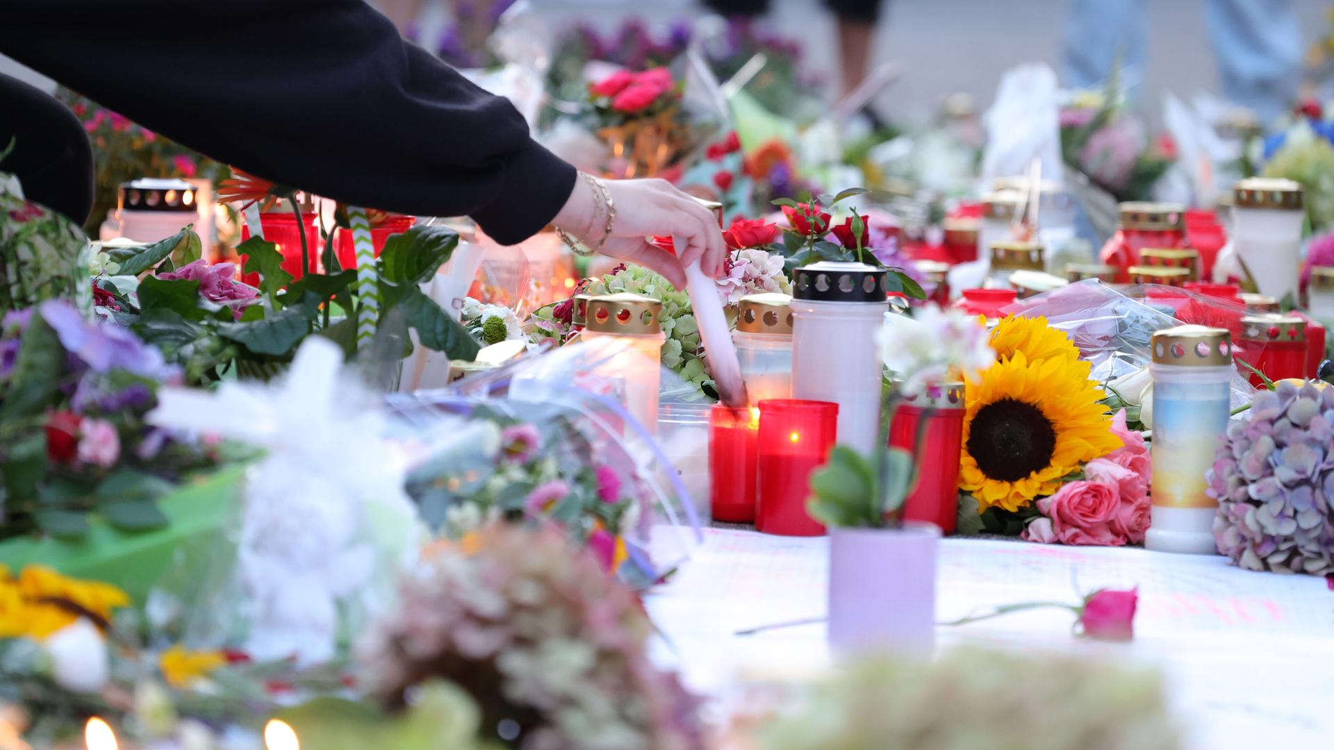 Blumen liegen in Solingen auf dem Boden. Daneben stehen Grablichter. Eine Hand hält eine weiße Kerze und zündet sie an. 