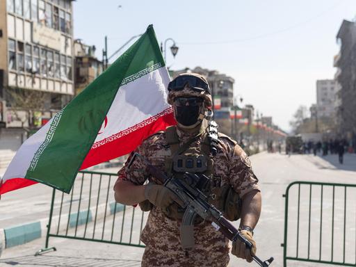 Ein Soldat der Iranischen Revolutionsgarde steht vor einer abgesperrten Straße, neben ihm weht die iranische Flagge Ein Soldat der Iranischen Revolutionsgarde steht vor einer abgesperrten Straße, neben ihm weht die iranische Flagge