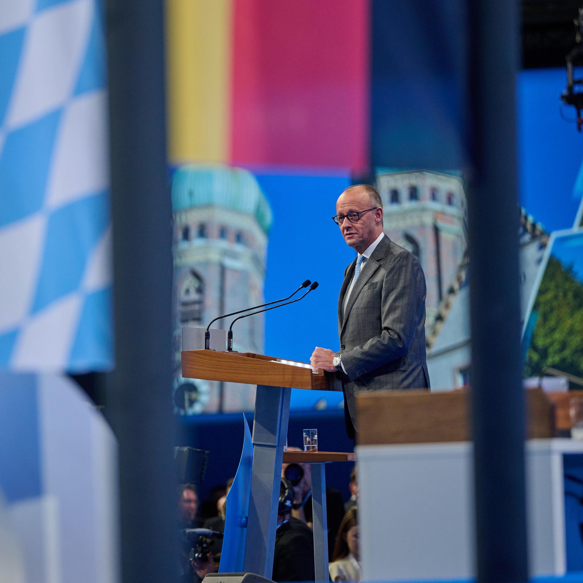 Bundeskanzler Friedrich Merz steht auf einer Bühne. Zu sehen sind die Flaggen Deutschlands und Bayerns.