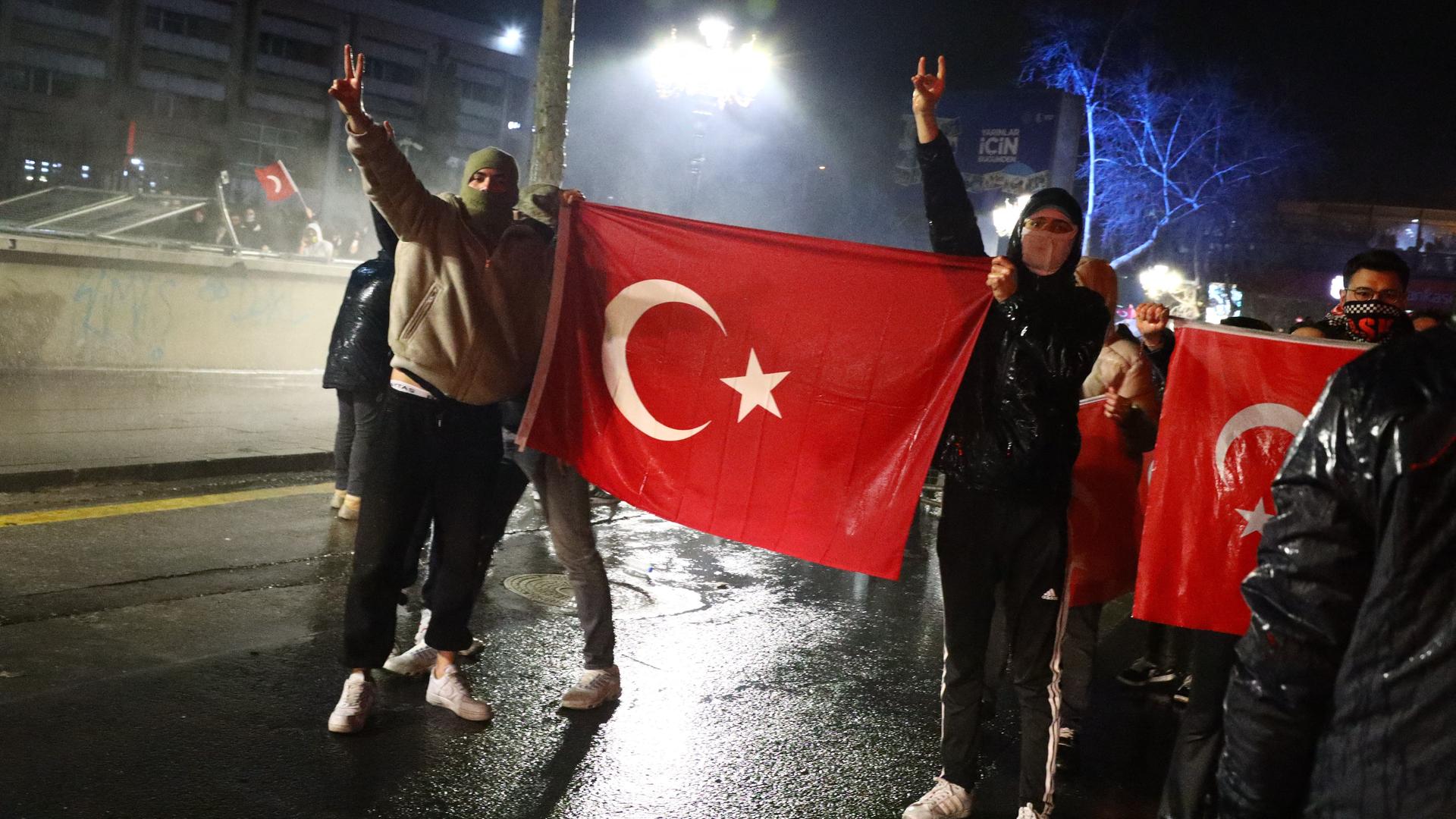 Zwei Protestierende halten eine Flagge der Türkei hoch und zeigen mit den Händen das Peace-Zeichen