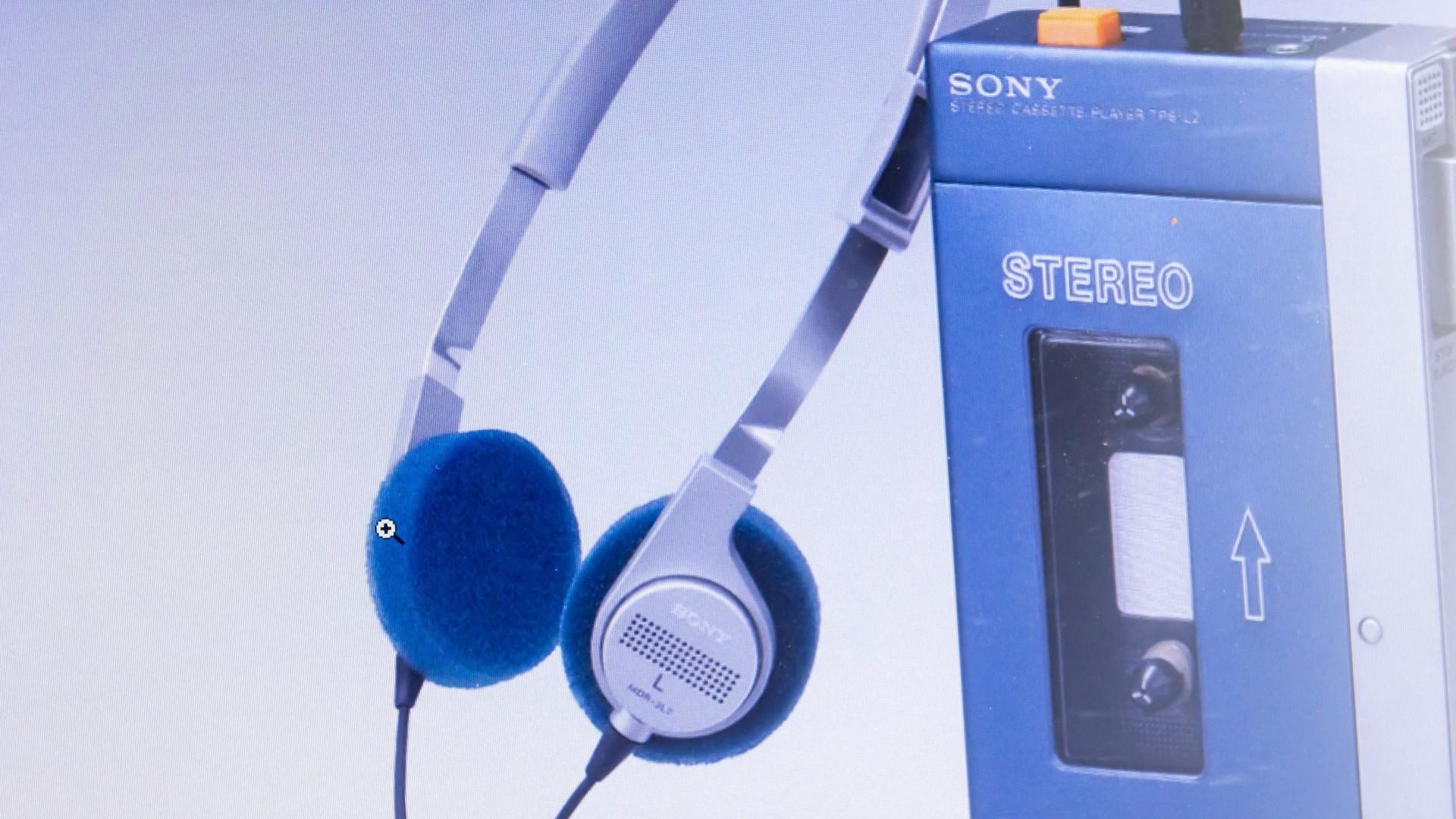 Auf dem Bild ist ein mobiles Kassettenabspielgerät der Firma Sony, ein sogenannter Walkman, zu sehen, daneben der dazugehörige Kopfhörer. Auf dem Bild ist ein mobiles Kassettenabspielgerät der Firma Sony, ein sogenannter Walkman, zu sehen, daneben der dazugehörige Kopfhörer.