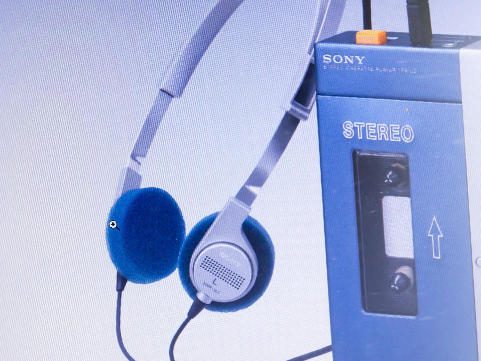 Auf dem Bild ist ein mobiles Kassettenabspielgerät der Firma Sony, ein sogenannter Walkman, zu sehen, daneben der dazugehörige Kopfhörer. 