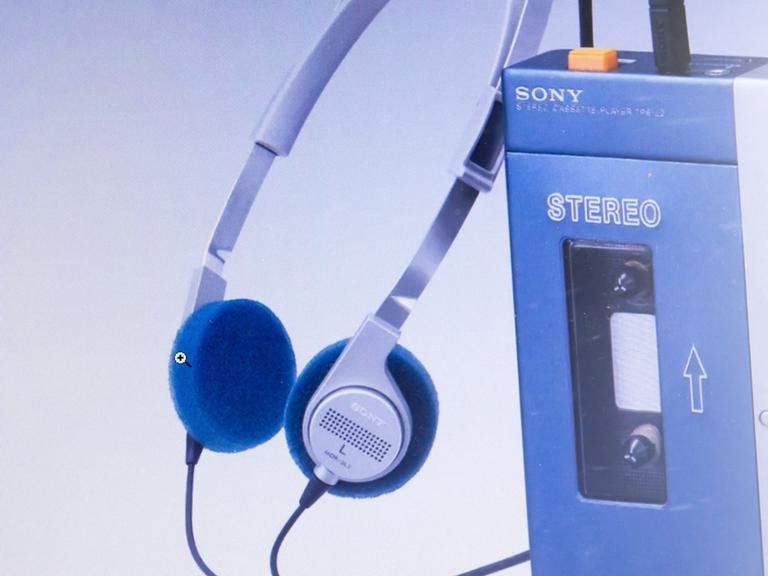 Auf dem Bild ist ein mobiles Kassettenabspielgerät der Firma Sony, ein sogenannter Walkman, zu sehen, daneben der dazugehörige Kopfhörer. 