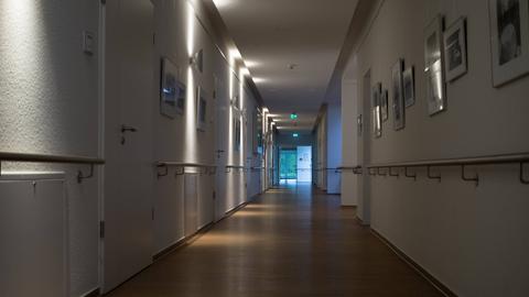 Blick durch einen Hospizflur an den geschlossenen Türen vorbei auf eine offene Tür, durch die man das Tageslicht sieht.