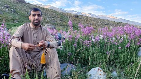 Der Übersetzer Jawed Haqmal in Afghanistan vor einer blühenden Wiese mit einer Berglandschaft im Hintergrund. 