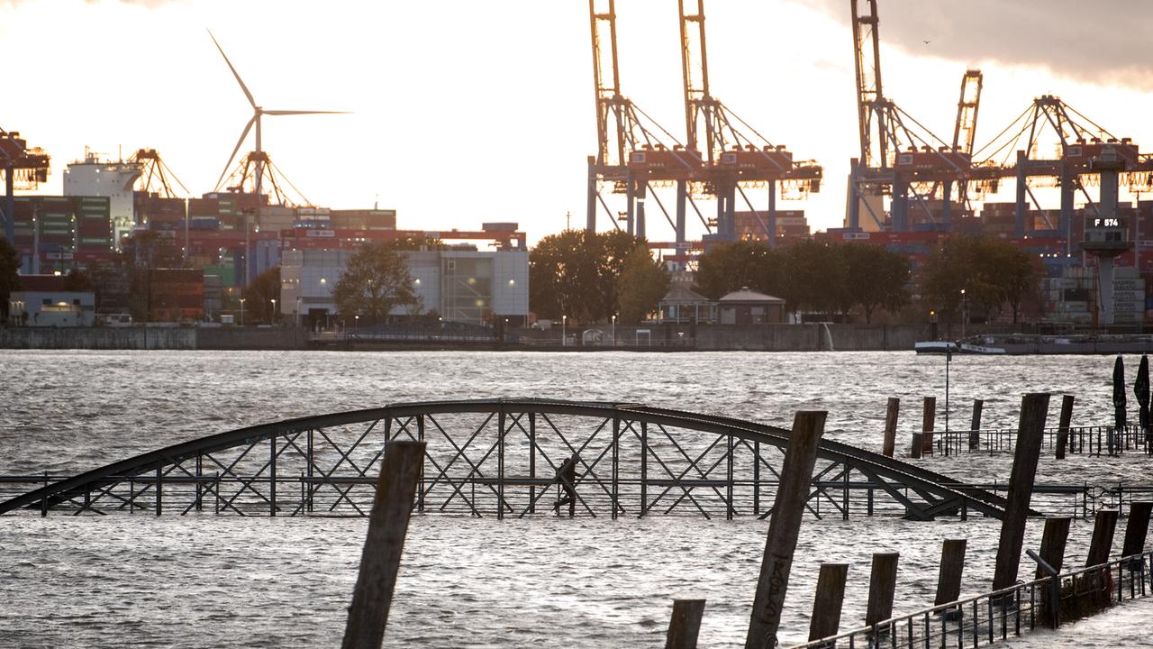 Eine Frau geht am Fischmarkt an der Elbe im Hafen während einer Sturmflut über eine unter Wasser stehende Brücke. Sturmtief „Joshua“ zog im Oktober 2025 als Herbststurm über Deutschland hinweg.