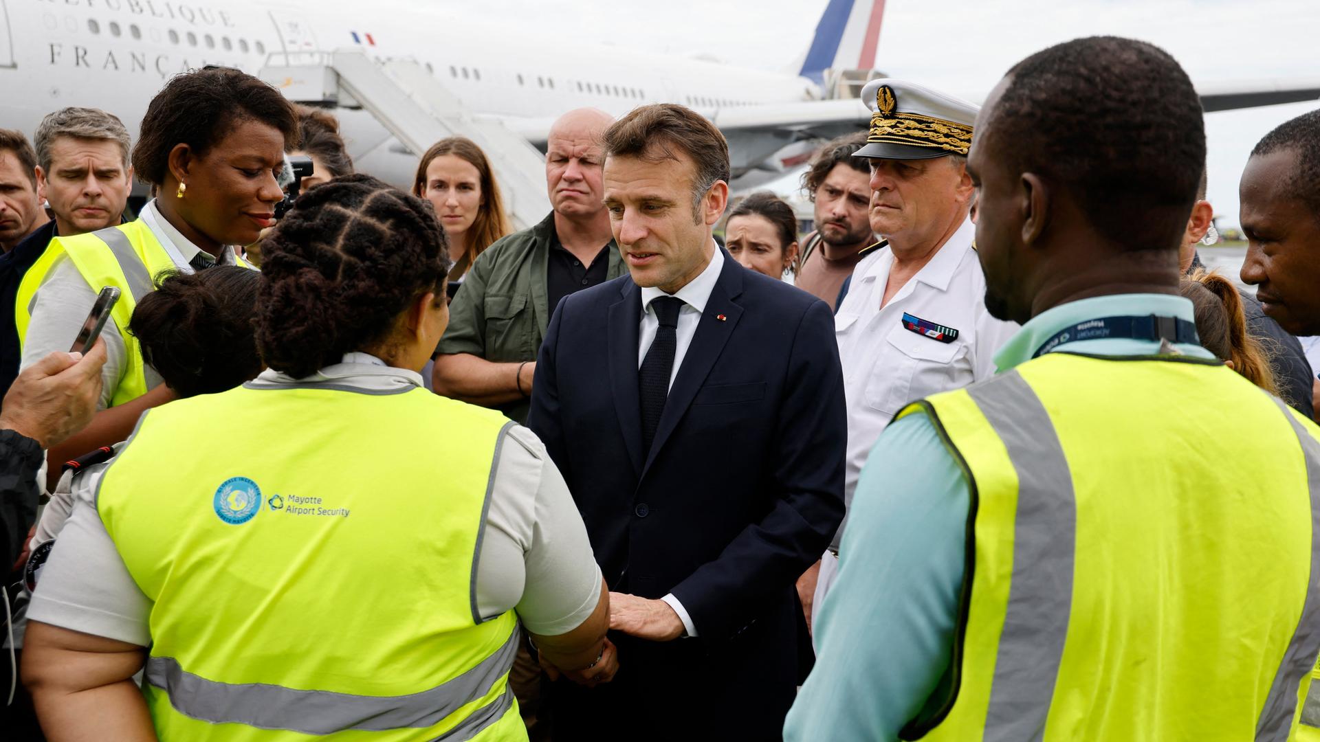 Frankreichs Präsident Macron wird von mehreren Personen am Flughafen begrüßt. 