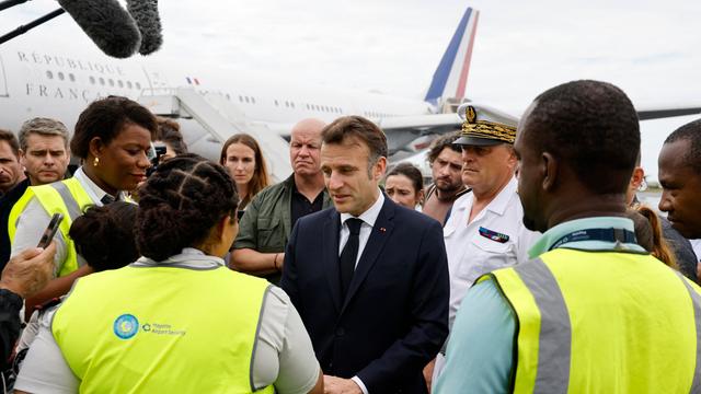 Frankreichs Präsident Macron wird von mehreren Personen am Flughafen begrüßt. 