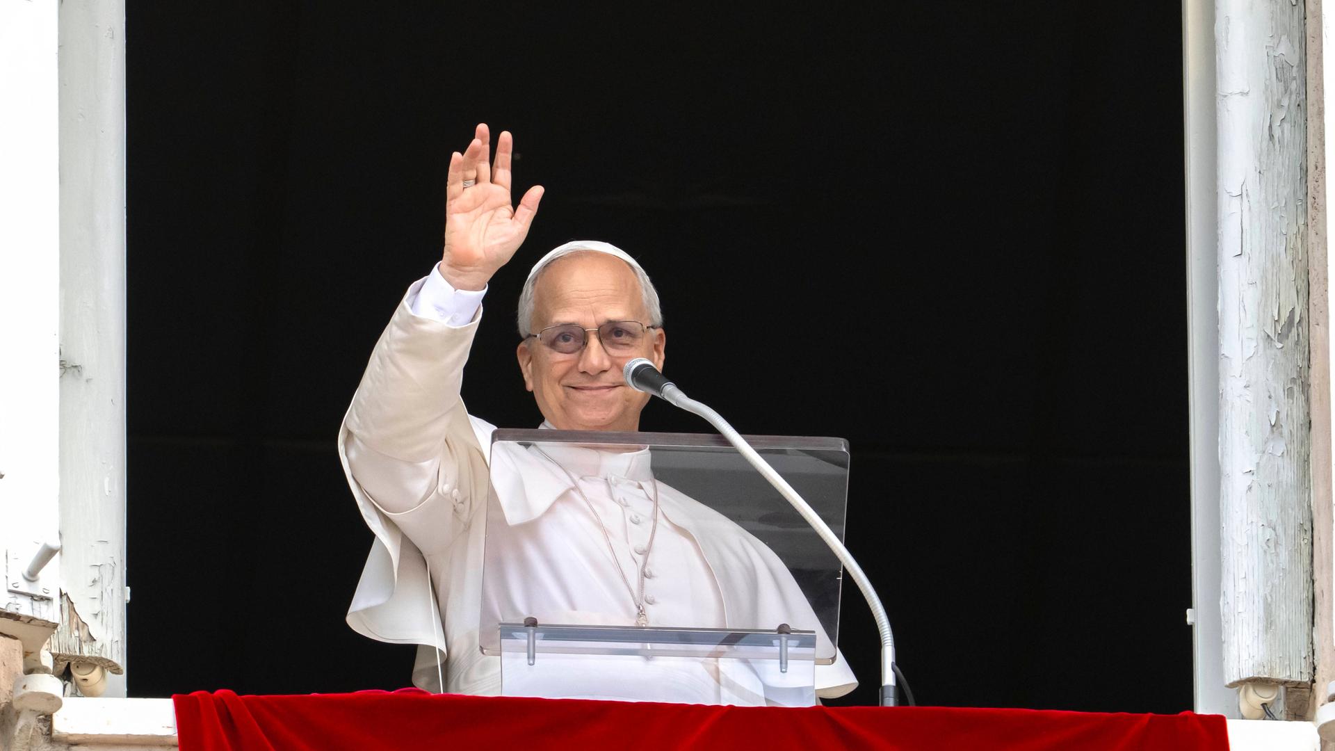 Das Foto zeigt Papst Leo am Fenster, er hält eine Hand zum Gruß hoch. VATICANxMEDIAx