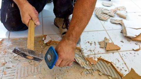 Ein Fliesenleger entfernt mit Hammer und alte Fliesen in einem Bad,