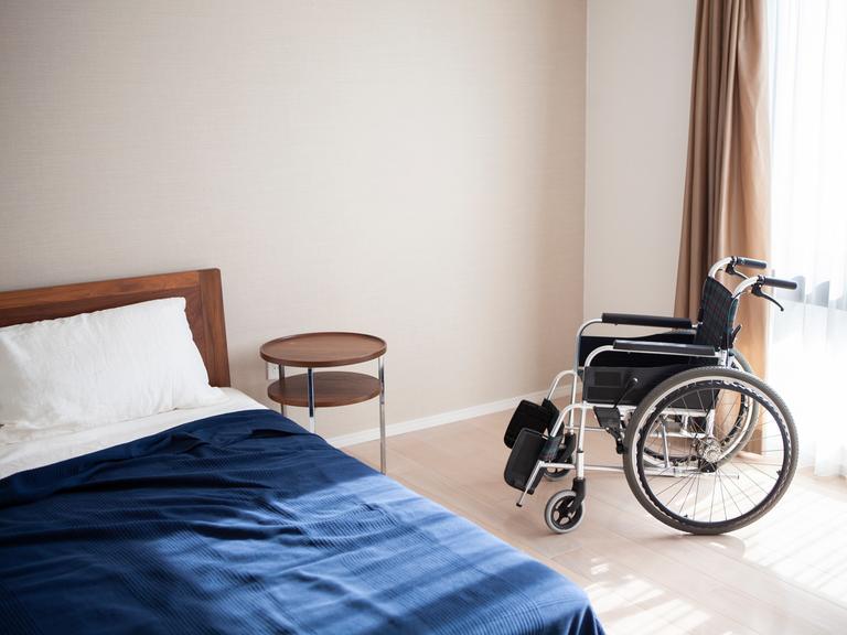 In einem Seniorenheim steht ein leerer Rollstuhl und ein leeres Bett. In einem Seniorenheim steht ein leerer Rollstuhl und ein leeres Bett.