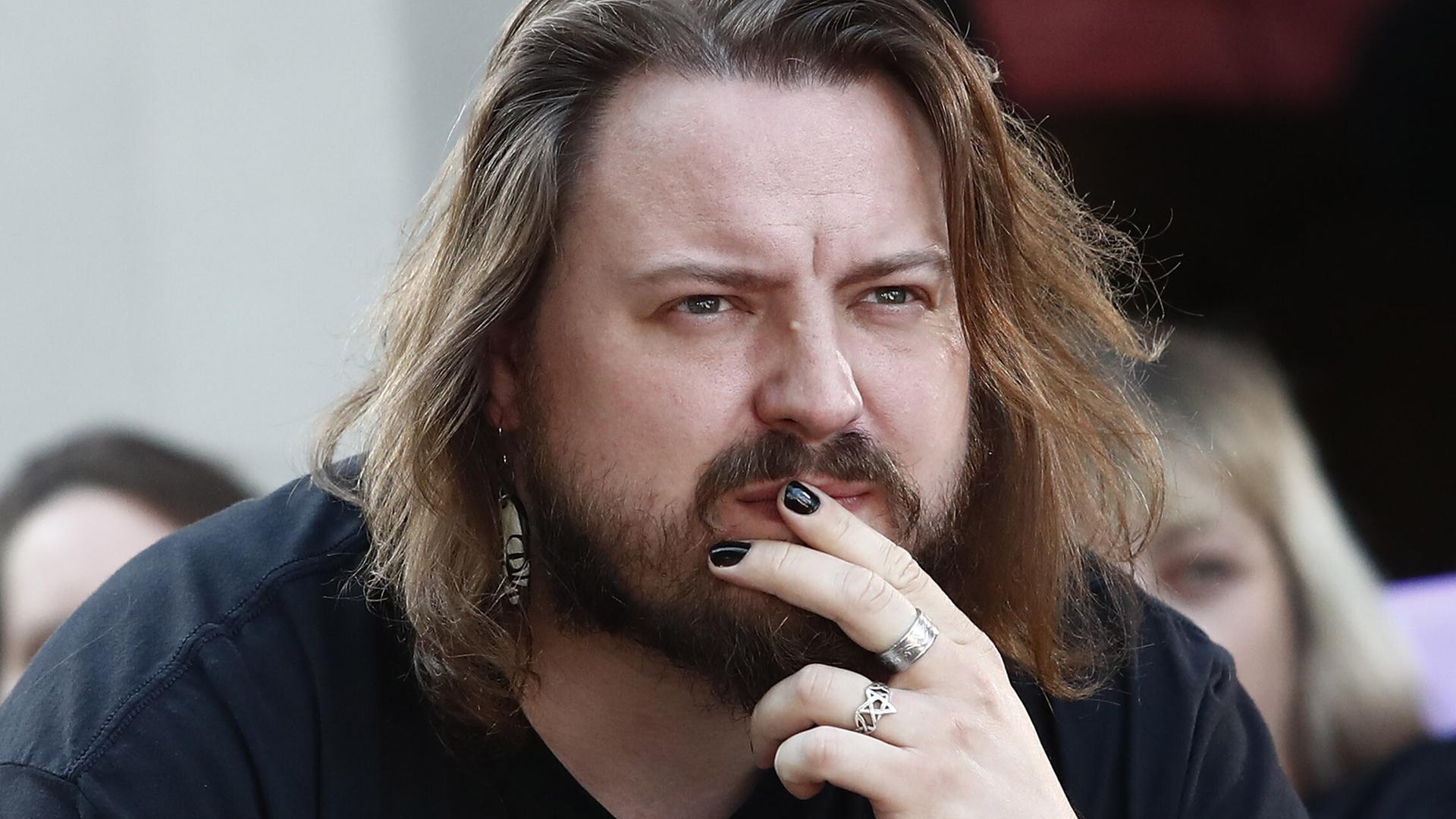 Martin Piekar legt die Hand an den Mund und blickt ernst ins Off. Er hat etwas längere Haare und einen Vollbart