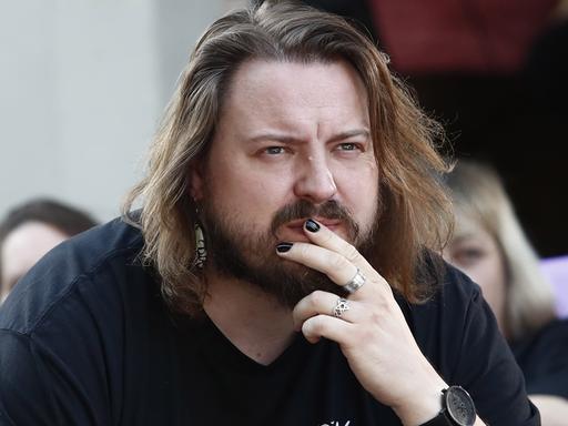Martin Piekar legt die Hand an den Mund und blickt ernst ins Off. Er hat etwas längere Haare und einen Vollbart