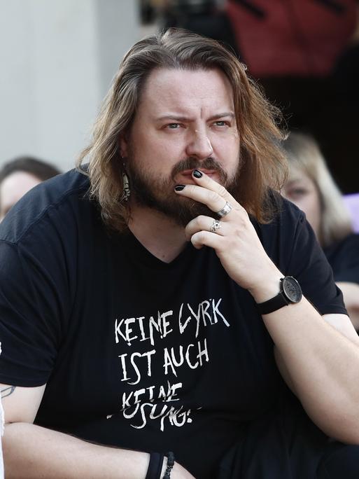 Martin Piekar legt die Hand an den Mund und blickt ernst ins Off. Er hat etwas längere Haare und einen Vollbart