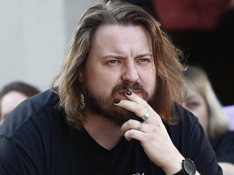 Martin Piekar legt die Hand an den Mund und blickt ernst ins Off. Er hat etwas längere Haare und einen Vollbart