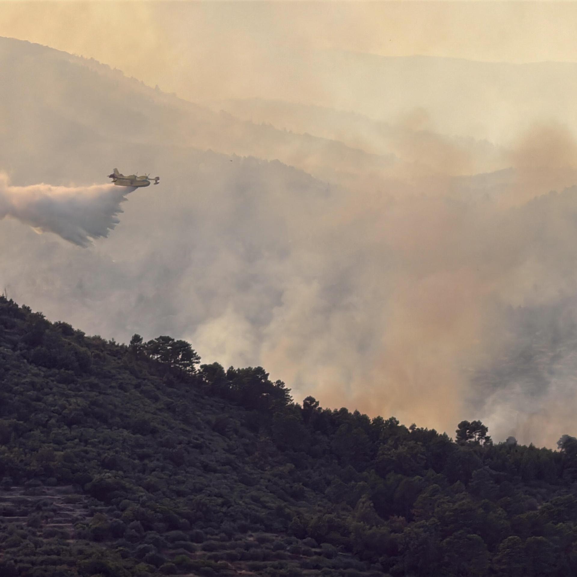 Ein Wasserwerfer-Flugzeug lässt Löschwasser über dem Wald im spanischen Avila ab.