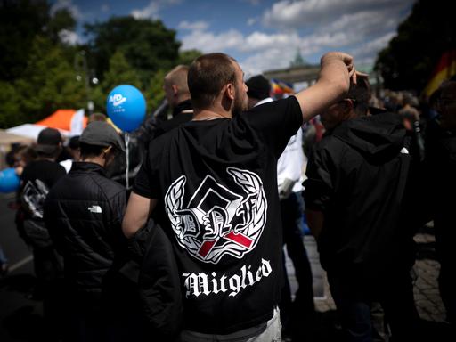 Blick auf eine Demonstration der als rechtsextrem eingestuften Partei AfD, der Querdenker-Bewegung und anderen rechten Gruppierungen. Im Vordergrund sieht man einen Demonstrant von hinten mit einem schwarzen T-Shirt mit einem Runenzeichen. 