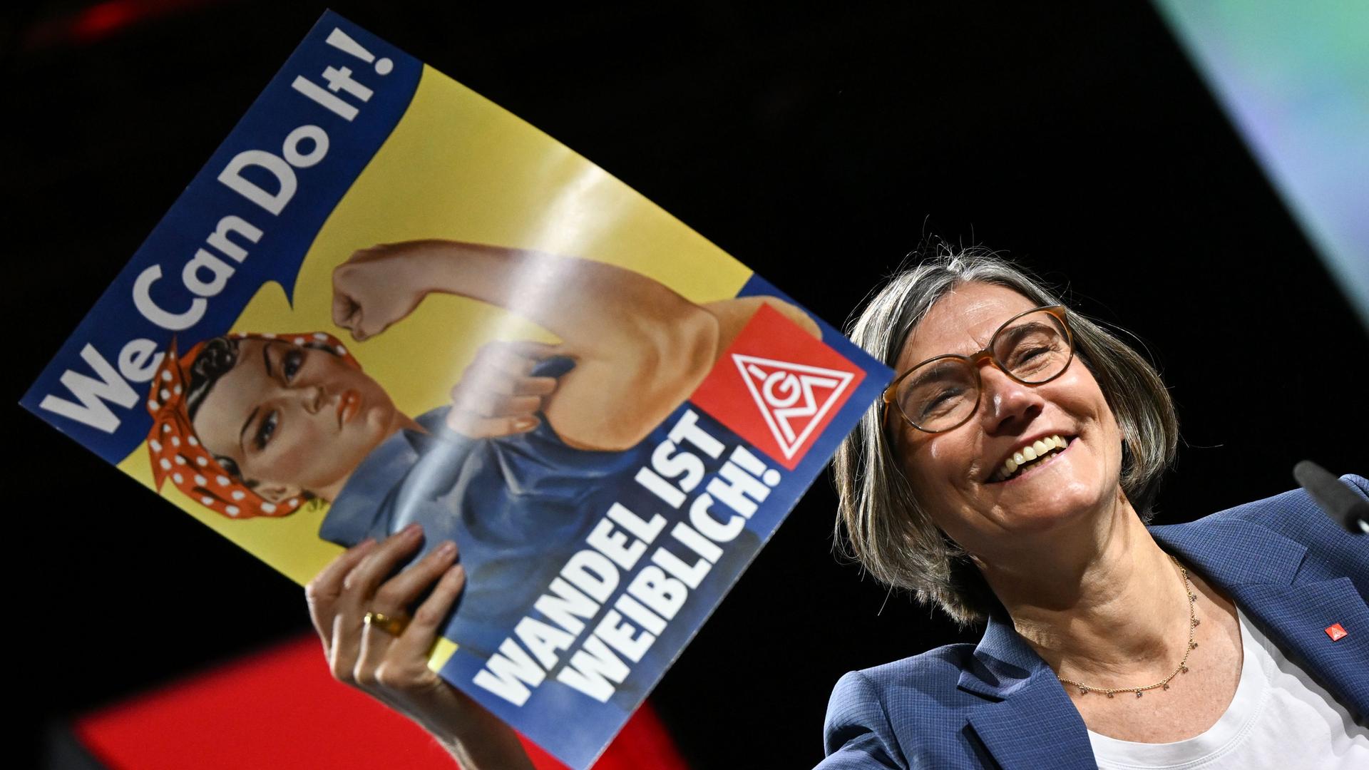 Das Foto zeigt die neue Vorsitzende von der Gewerkschaft IG Metall. Christiane Benner hält ein Plakat in der Hand. 