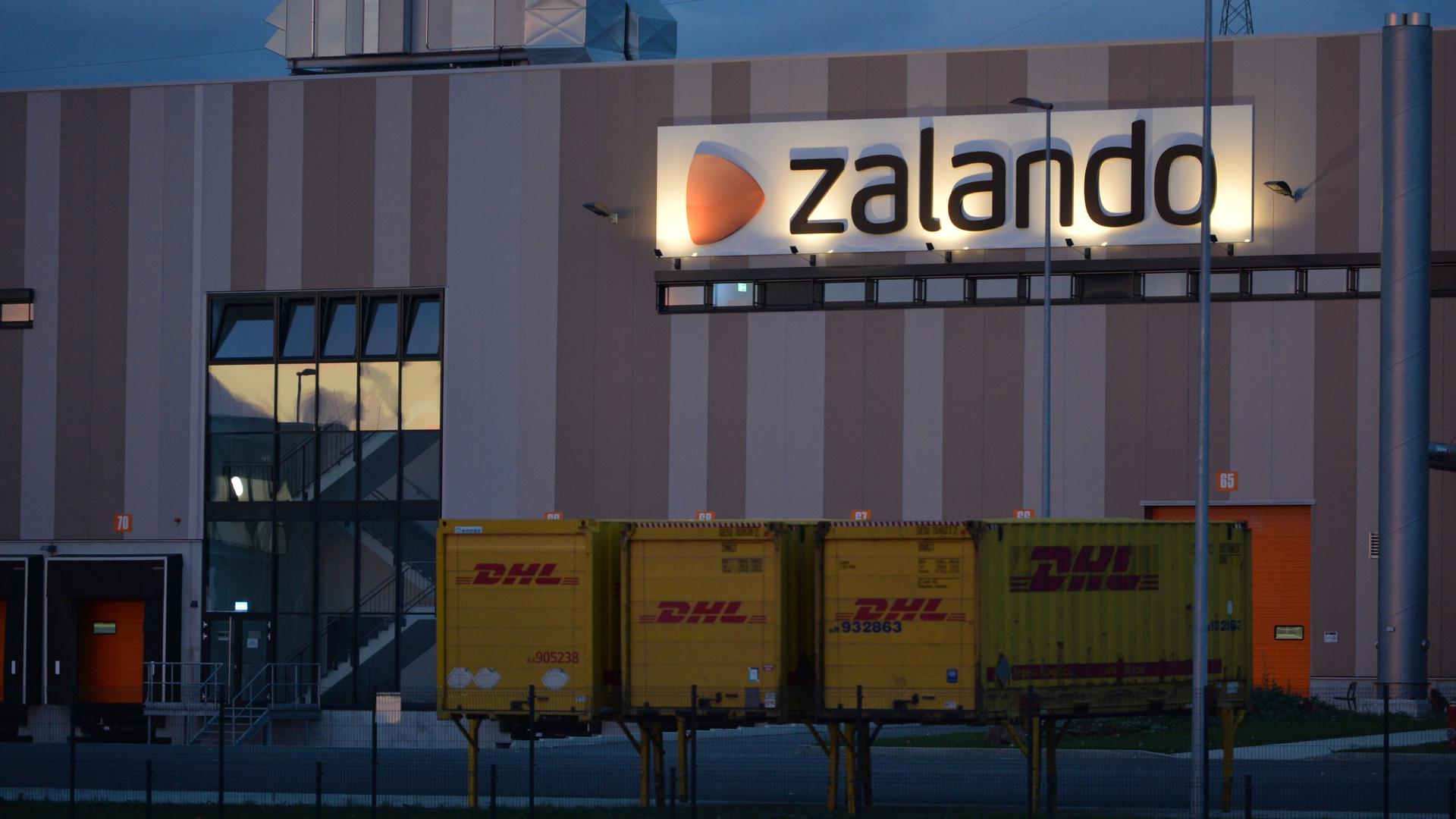 Das Logistikzentrum des Onlinehändlers Zalando, davor stehen drei DHL-Container.