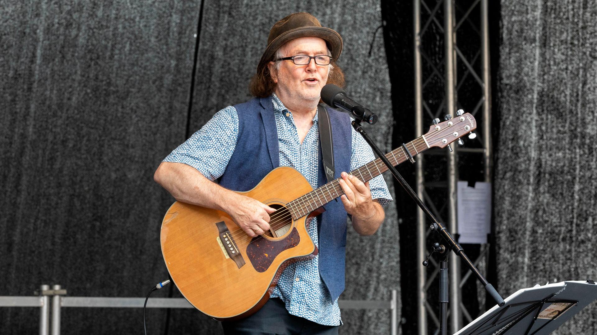 Der Musiker Gerhard Schöne bei einen Konzert auf einer Bühne am Mikrofon singend und Gitarre spielend