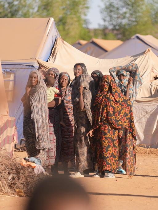 Mehrere Frauen im Flüchtlingslager Goz al-Haj blicken skeptisch in die Kamera, im Hintergrund Zelte. 