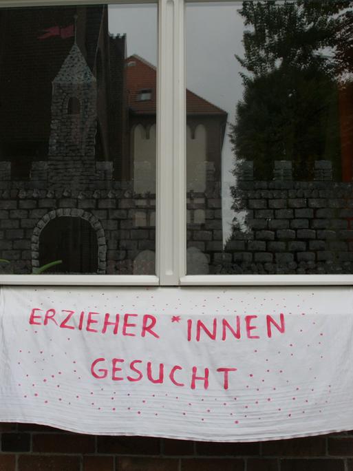 Ein Transparent auf dem geschrieben steht, "Erzieher*innen gesucht" an einer Häuserwand aus Backstein in Berlin.
