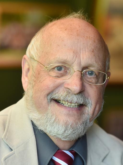 Tom Hoyem lächelt in die Kamera. Er trägt eine Brille mit schmalem goldenen Rand und hat einen gestutzten weißen Vollbart.