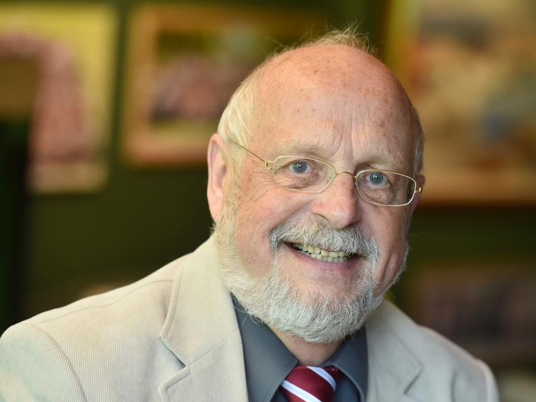 Tom Hoyem lächelt in die Kamera. Er trägt eine Brille mit schmalem goldenen Rand und hat einen gestutzten weißen Vollbart.