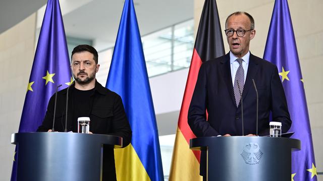 Wolodymyr Selenskyj und Friedrich Merz stehen nebeneinander vor 2 Pulten. 