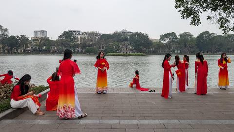 Mehrere Frauen in traditionellen rot-gelben Kleider posieren an einem Seeufer für Fotos.