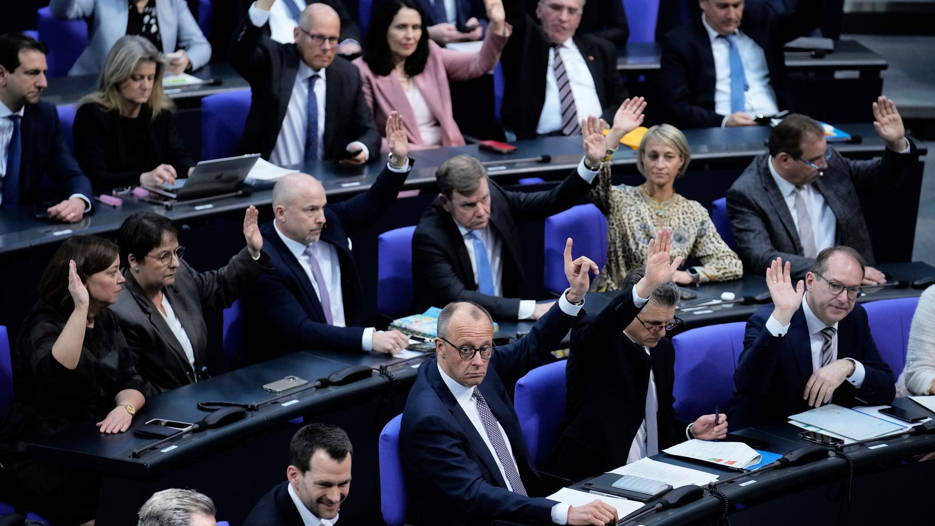 Mehrere Politiker sitzen in dem Bundestag. Sie haben ihre Hand zur Abstimmung.