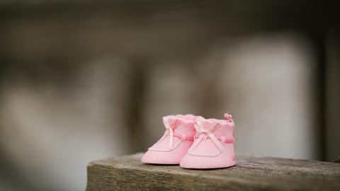Ein rosa farbenes Paar Babyschuhe steht auf einem Holzregal.