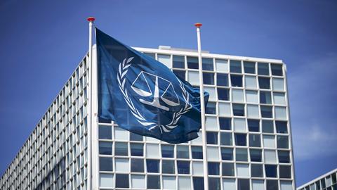 Außenansicht des Internationalen Strafgerichtshofs (IStGH) vor blauem Himmel und Flagge im Vordergrund.