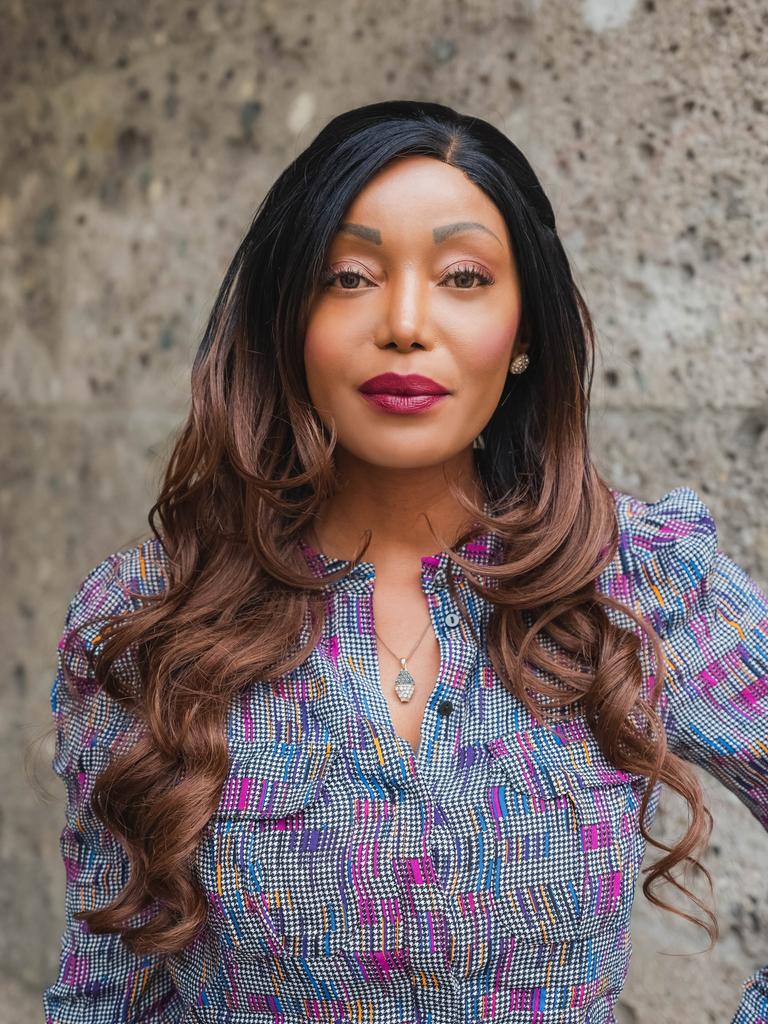 Porträt von Irène Kilubi. Sie trägt eine gemusterte Bluse und lange dunkelbraune Locken.