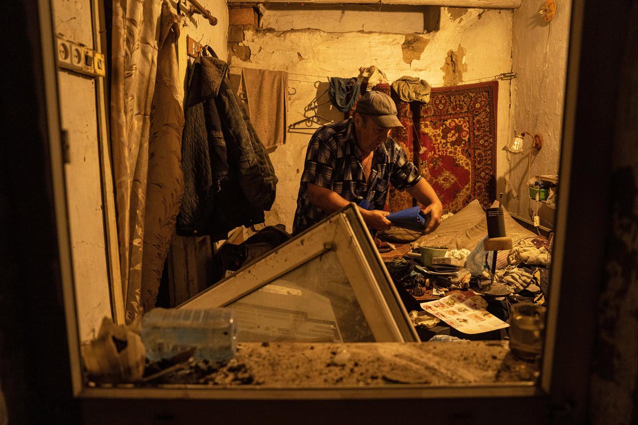 Eine zerstörte Wohnung in einem Haus in der ukrainischen Stadt Pokrowsk nach einem russsichen Raketenangriff im Juni 2023. Das Fenster ist aus dem Rahmen gefallen, das Zimmer verwüstet. Ein Mann sammelt Dokumente ein. 