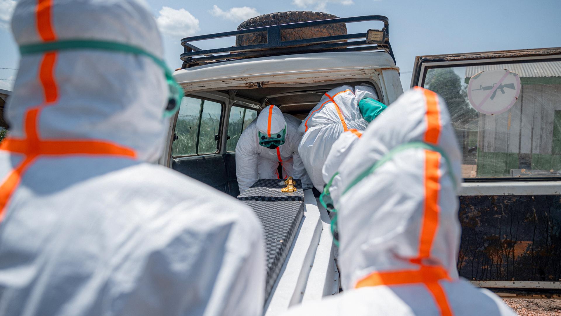 Mitarbeiter des Gesundheitswesens in Schutzkleidung heben den Sarg eines Verstorbenen in einen Transporter.