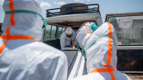 Mitarbeiter des Gesundheitswesens in Schutzkleidung heben den Sarg eines Verstorbenen in einen Transporter.