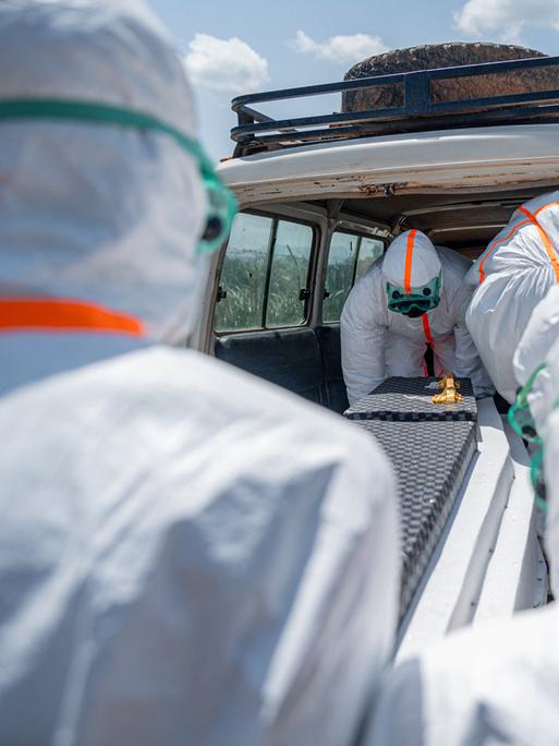 Mitarbeiter des Gesundheitswesens in Schutzkleidung heben den Sarg eines Verstorbenen in einen Transporter.