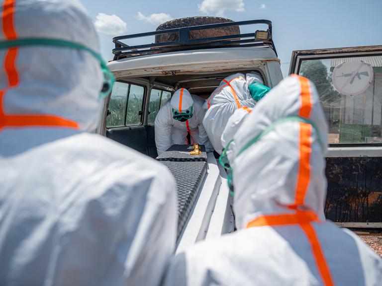 Mitarbeiter des Gesundheitswesens in Schutzkleidung heben den Sarg eines Verstorbenen in einen Transporter.