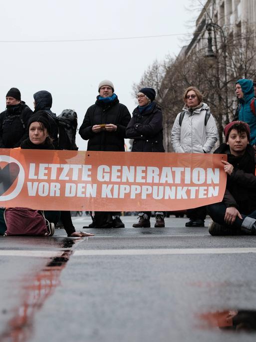 Mehrere Menschen blockieren eine Straße in Berlin mit einem Transparent, auf dem steht: "Letzte Generation vor den Kipppunkten".