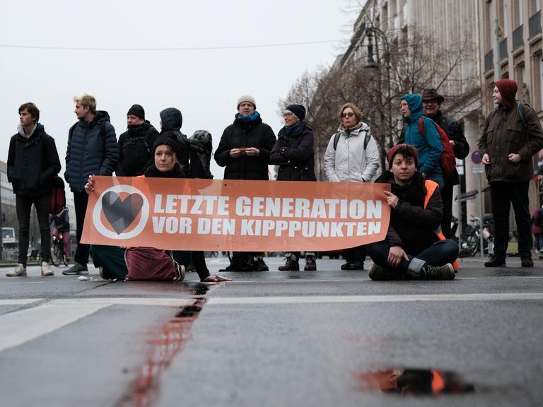 Mehrere Menschen blockieren eine Straße in Berlin mit einem Transparent, auf dem steht: "Letzte Generation vor den Kipppunkten".