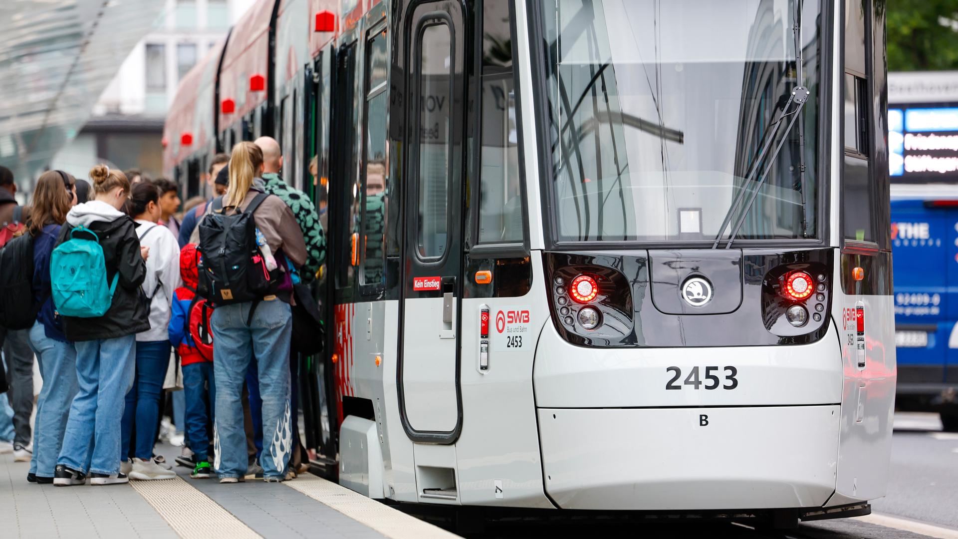 Menschen steigen an einer Haltestelle in die Straßenbahn ein. 