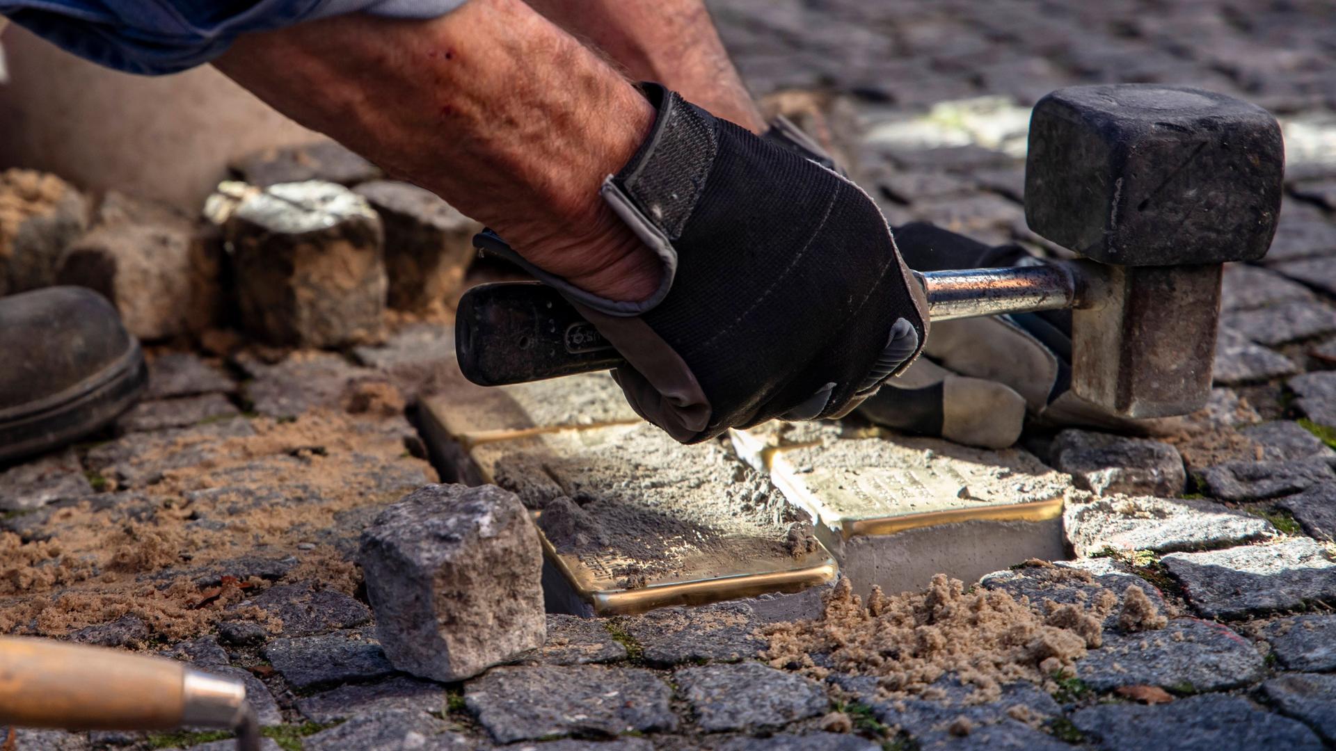 Blick auf Hände, die gerade Verlegearbeiten von Stolpersteinen erledigen. Blick auf Hände, die gerade Verlegearbeiten von Stolpersteinen erledigen.