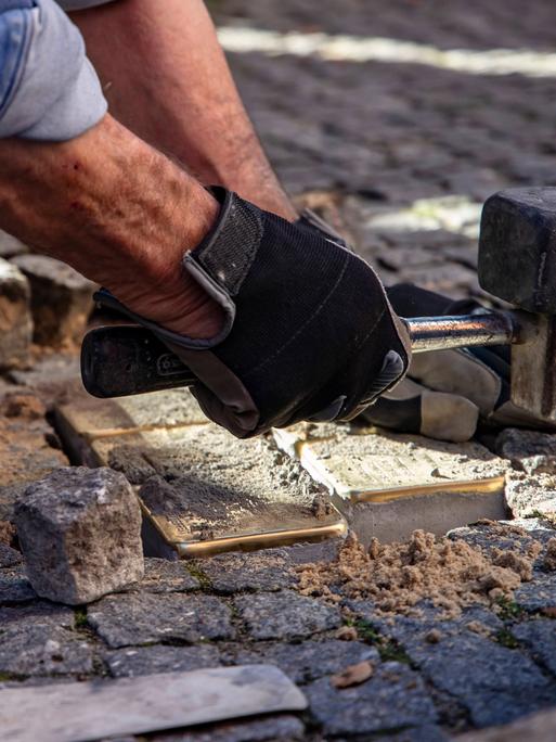 Blick auf Hände, die gerade Verlegearbeiten von Stolpersteinen erledigen.
